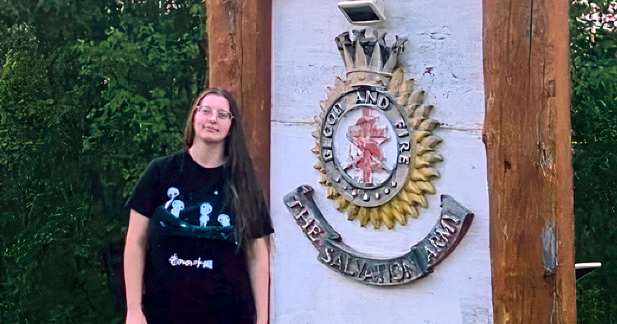 Teen girl standing beside a sign with a Salvation Army crest on it